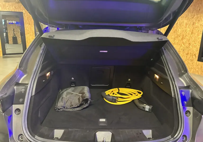 Coffre ouvert d’un Alfa Romeo Tonale gris foncé 2023, montrant un câble de recharge jaune et un sac noir à l’intérieur.