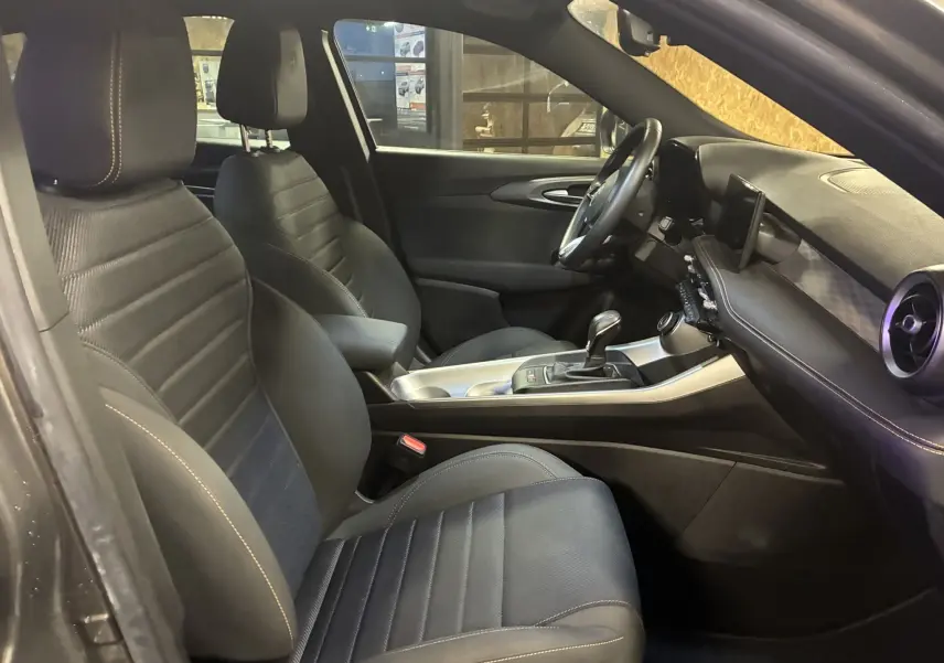 Vue intérieure côté conducteur de l'Alfa Romeo Tonale gris foncé 2023, sièges noirs avec surpiqûres contrastées.