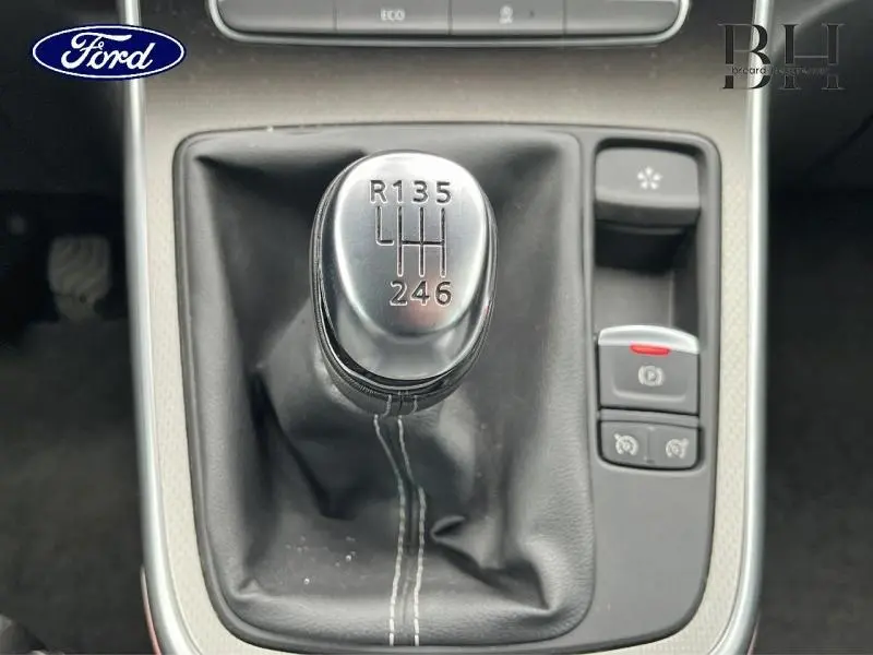 Gros plan sur le levier de vitesses manuel en métal et cuir noir de la Renault Scénic blanc nacré, avec commandes électroniques adjacentes.