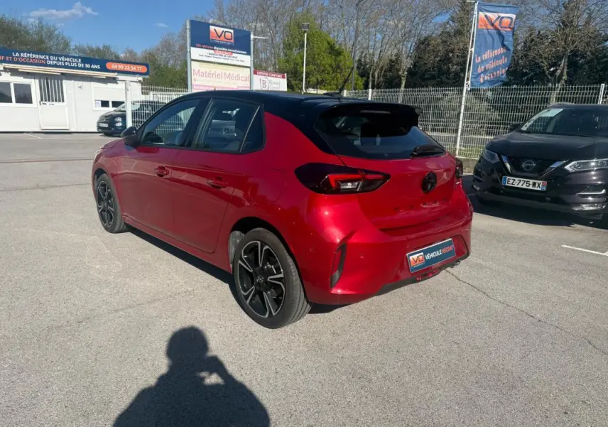 Vue 3/4 arrière droite d'une Opel Corsa rouge 2025 avec toit noir et jantes alliage noires sur parking.