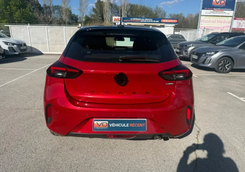 Vue arrière d'une Opel Corsa rouge 2025 avec badge Hybrid et plaque Véhicule Récent sur un parking extérieur.