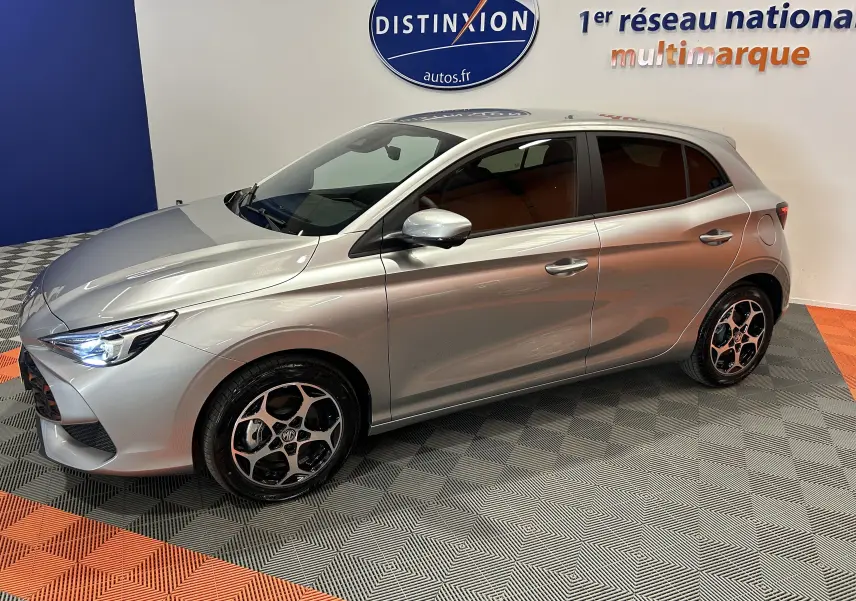 Vue 3/4 avant droit de la MG3 Cosmic Silver 2026, hybride, avec jantes distinctives et phares LED allumés.