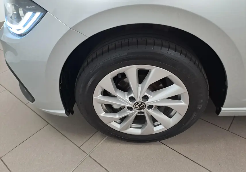 Gros plan sur la roue avant gauche et le phare allumé d'une Volkswagen Polo 1.0 TSI Style argentée.
