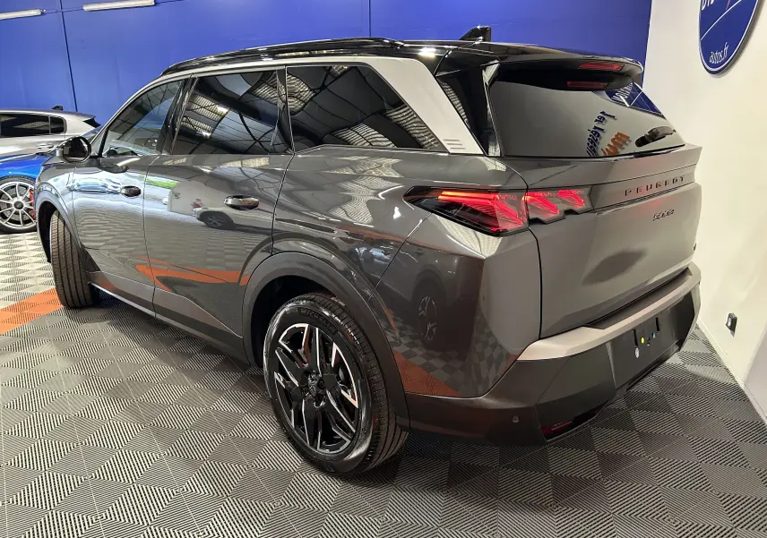 Vue 3/4 arrière droite d’un Peugeot 5008 gris titane avec hayon électrique et jantes noires brillantes.
