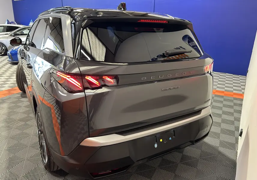 Vue 3/4 arrière droite du Peugeot 5008 gris titane avec feux arrière LED allumés dans un showroom.