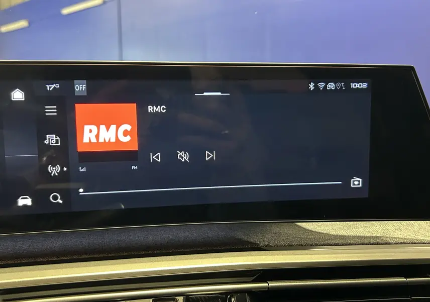 Écran tactile intérieur du Peugeot 5008 Hybrid gris titane affichant la radio RMC, vue frontale.