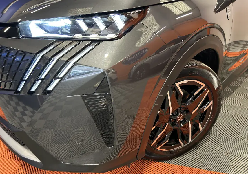 Gros plan sur l’avant droit gris titane du Peugeot 5008 Hybrid 145ch GT, mettant en valeur le phare LED et la jante noire stylisée.