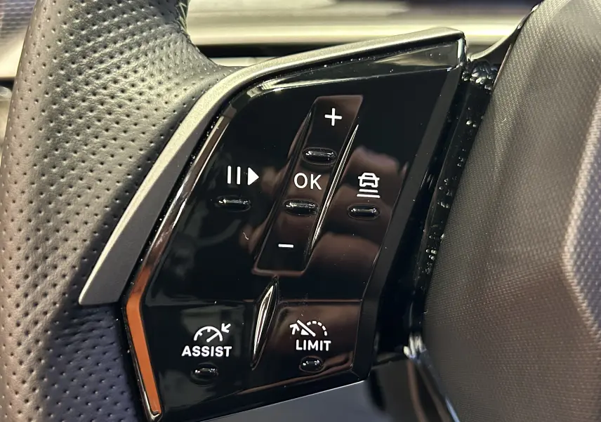 Gros plan sur les commandes noires au volant du Peugeot 5008 Hybrid gris titane, avec boutons de régulateur et assistant.