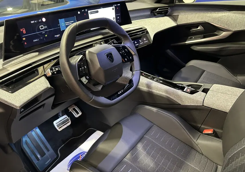 Vue intérieure côté conducteur du Peugeot 5008 Hybrid gris titane, avec tableau de bord numérique et volant compact multifonction.