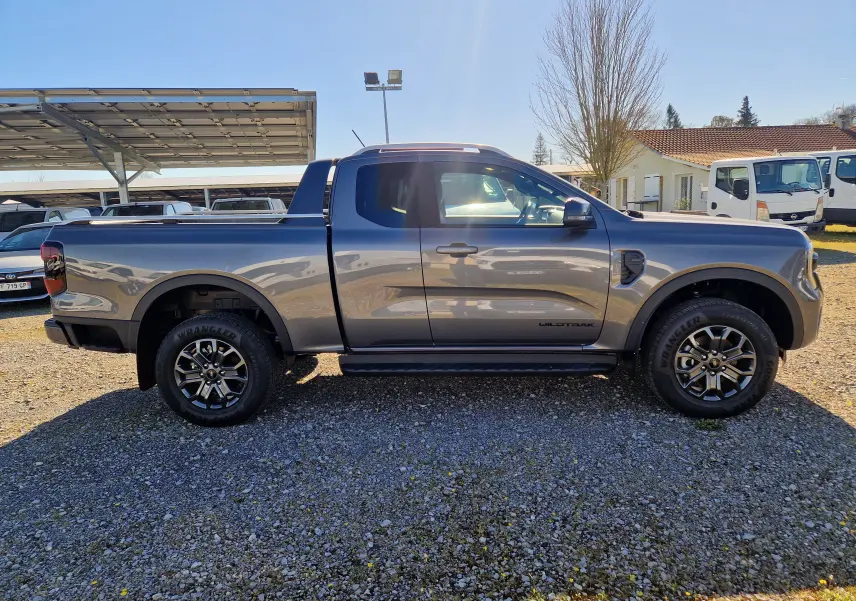 Vue de profil côté gauche du Ford Ranger Super Cabine gris carbone, avec jantes noires et badge Wildtrak visible.