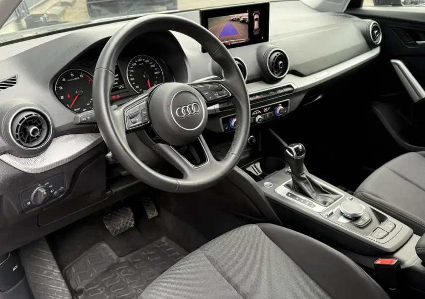 Vue intérieure côté conducteur de l'Audi Q2 2023 S line, tableau de bord moderne avec écran multimédia et boîte auto.