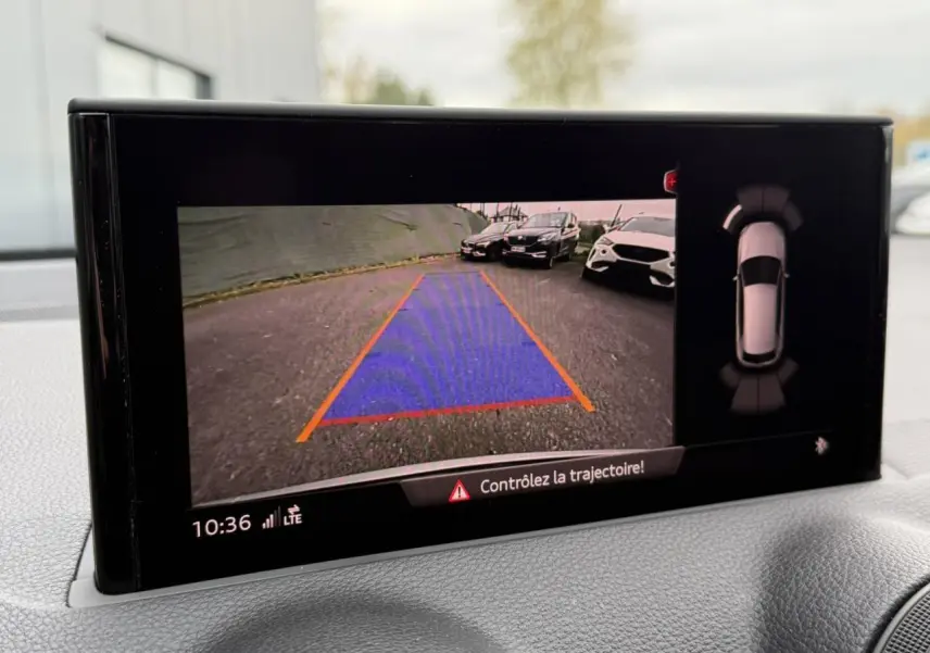 Affichage caméra de recul avec vue arrière du parking et alertes sur l'écran du tableau de bord d'un Audi Q2 noir métallisé S line.