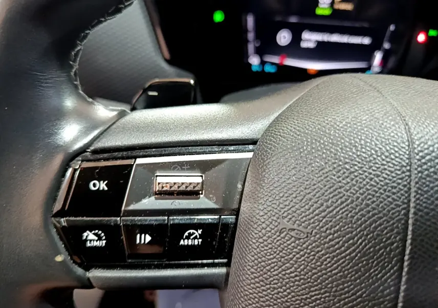 Gros plan sur les commandes gauche du volant cuir noir du DS4 E-TENSE 2023 avec affichage digital flou en arrière-plan