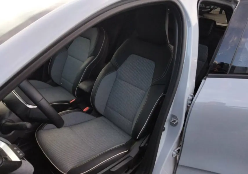 Vue intérieure côté conducteur de la Renault Clio gris rafale 2025, montrant les sièges en tissu et cuir avec surpiqûres blanches.