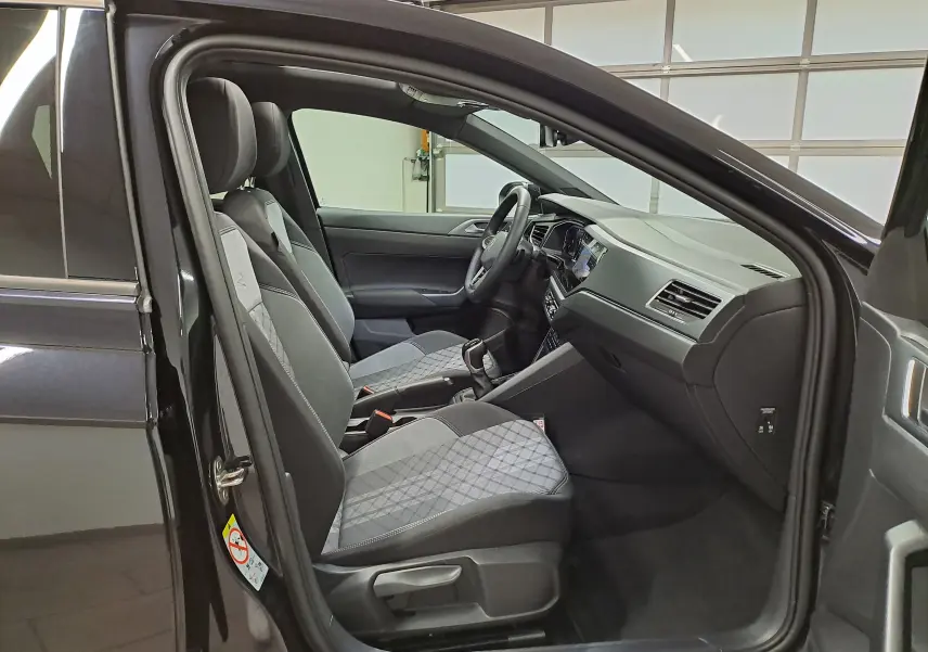 Vue intérieure côté conducteur du Volkswagen Taigo noir intense nacré, avec sièges sport en tissu et tableau de bord moderne.