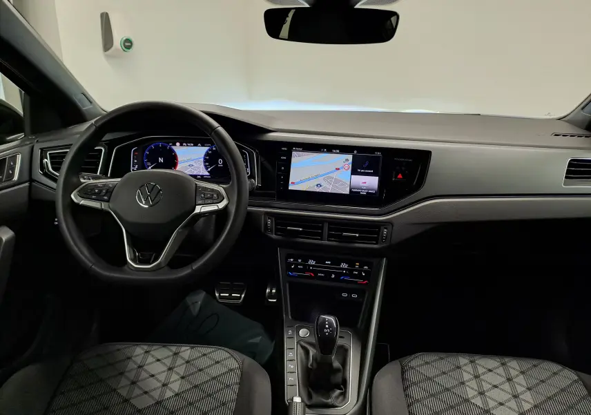 Vue intérieure avant du Volkswagen Taigo 1.5 TSI R-Line 2025, tableau de bord noir avec écran tactile et volant multifonctions.