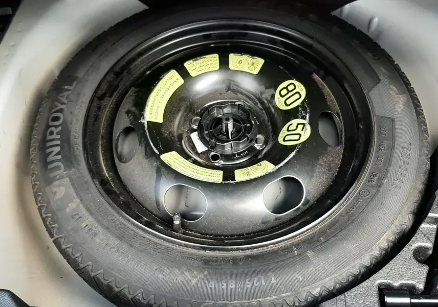 Roue de secours noire avec marquages jaunes dans le coffre d'un Peugeot 2008 blanc de 2021.