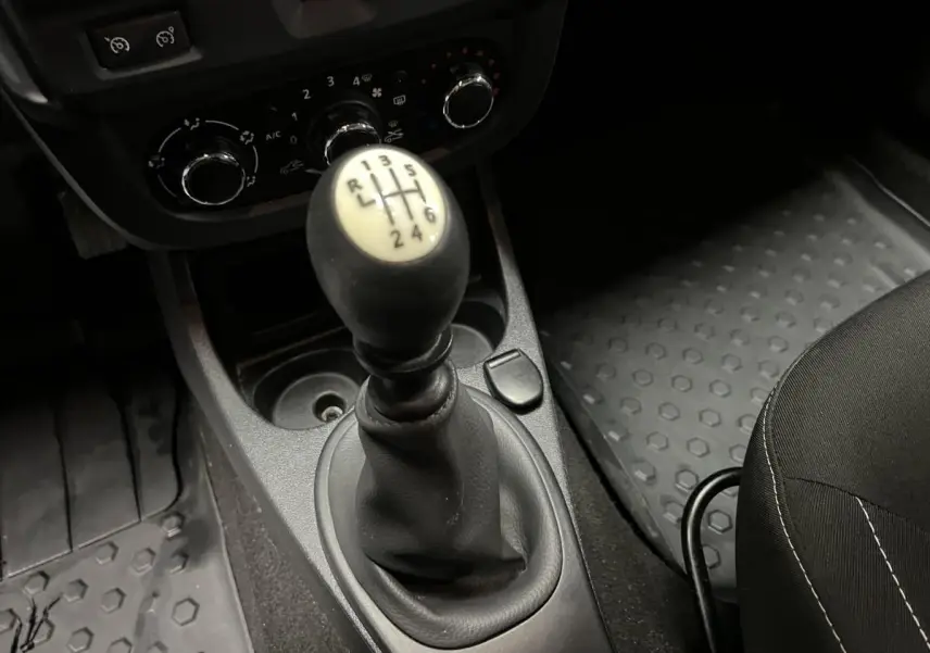 Le levier de vitesses manuel noir et beige du Dacia Duster 2016, entouré de commandes de climatisation et tapis caoutchouc.