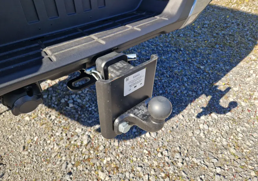 Gros plan sur l'attelage arrière noir du Ford Ranger Super Cabine gris Iconic, avec prise électrique visible sur sol gravillonné.