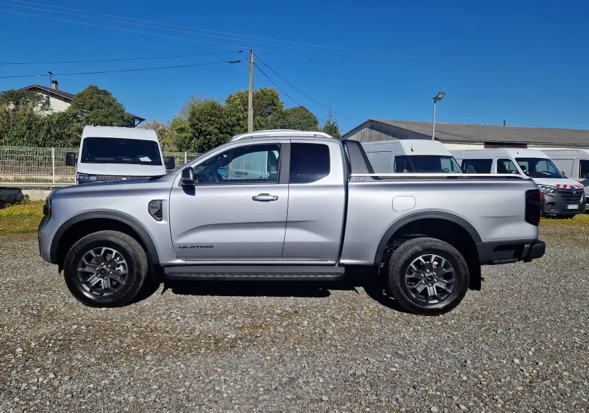 Vue de profil côté gauche d'un Ford Ranger Super Cabine Wildtrak gris iconic, avec jantes alliage et benne ouverte.
