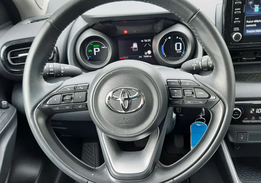 Vue intérieure centrée sur le volant noir de la Toyota Yaris 1.5 Hybrid 2023 avec tableau de bord digital et écran tactile.