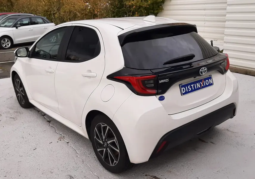 Vue 3/4 arrière droite d'une Toyota Yaris blanche 2023 avec toit et hayon noirs, jantes alliage bi-ton et vitres teintées.