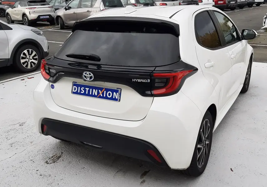 Vue 3/4 arrière droite d'une Toyota Yaris blanche hybride 2023 avec toit noir et feux arrière LED distinctifs.