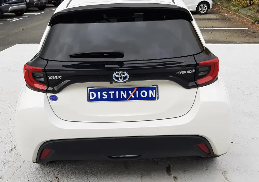Vue arrière d'une Toyota Yaris blanche hybride 2023 avec toit noir et feux arrière rouges distinctifs.