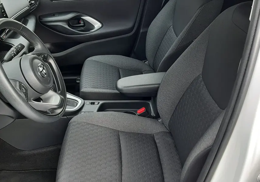 Vue intérieure côté conducteur de la Toyota Yaris blanche 2023, sièges tissu noir avec accoudoir central et volant multifonction.
