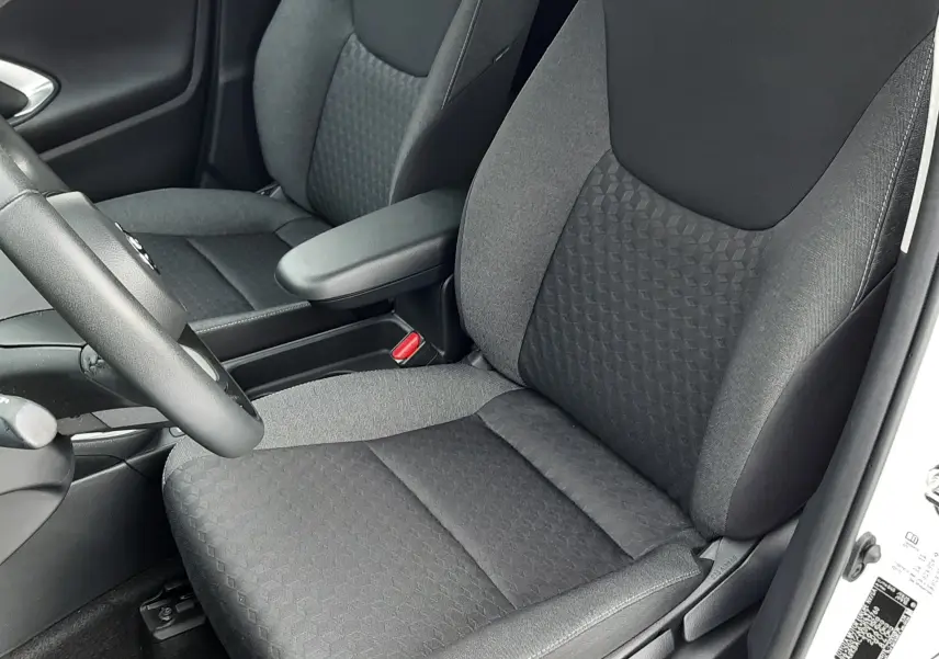 Vue intérieure côté conducteur de la Toyota Yaris 2023, sièges tissu noir avec accoudoir central et volant partiel visible.