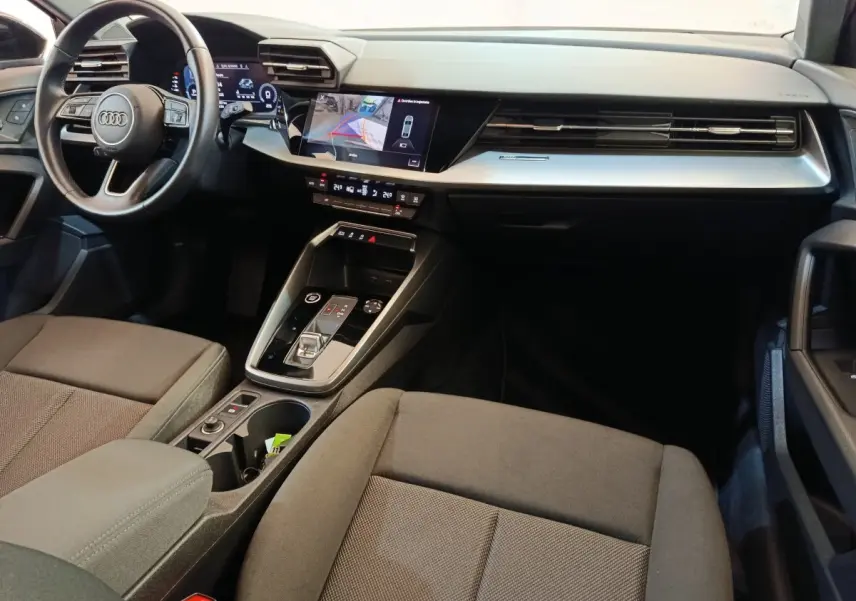 Intérieur de l'Audi A3 2022 noir, vue côté passager avant, tableau de bord moderne avec écran tactile et volant cuir.