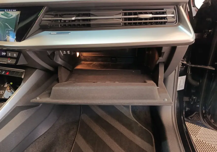 Vue intérieure côté passager de l'Audi A3 30 TFSI MHEV noire, boîte à gants ouverte et tableau de bord moderne.