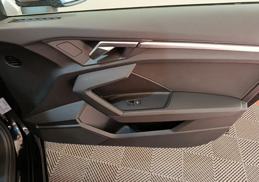 Vue rapprochée de la porte côté gauche noire de l'Audi A3 30 TFSI MHEV avec poignée argentée et commande de fenêtre.