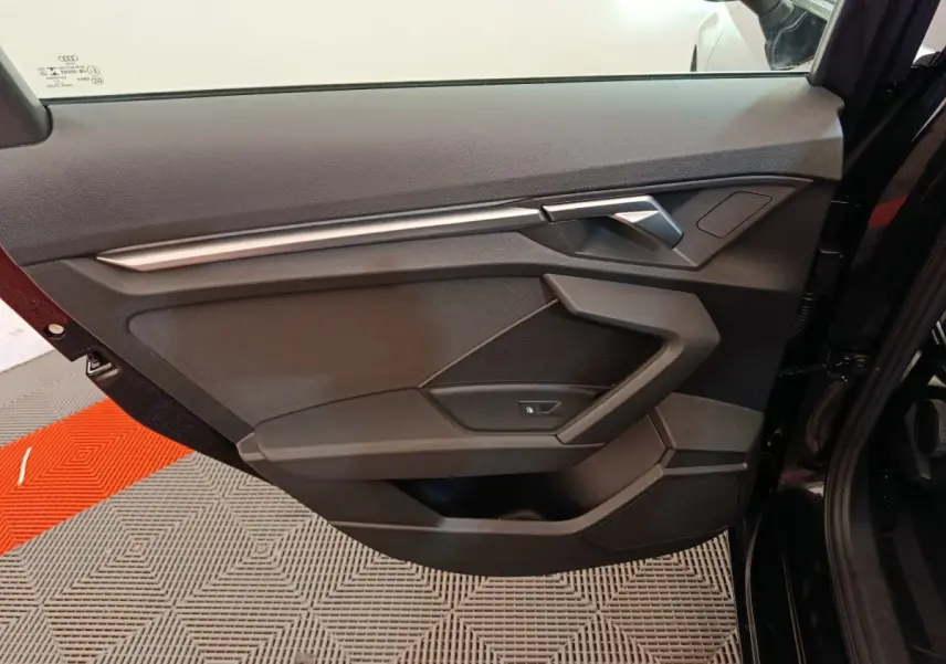 Porte intérieure côté gauche noire de l'Audi A3 30 TFSI MHEV Business Line 2022 avec poignée argentée et commande de vitre.