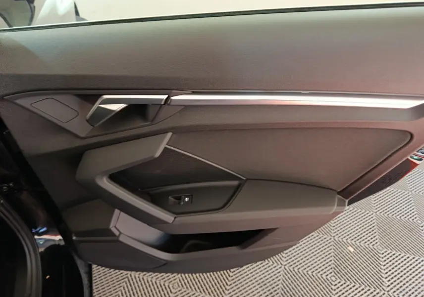 Vue rapprochée de la porte côté gauche noire de l'Audi A3 30 TFSI MHEV avec poignée et commande de vitre intégrées.