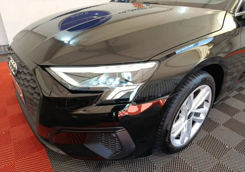 Vue 3/4 avant droit d'une Audi A3 noire 2022 mettant en valeur ses phares LED et sa calandre hexagonale distinctive.