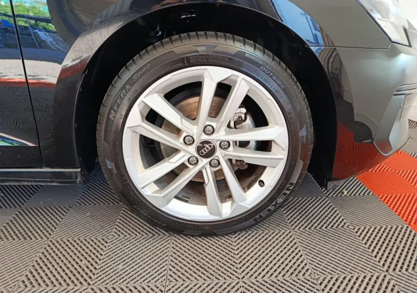 Gros plan sur la roue avant gauche d'une Audi A3 noire, mettant en valeur la jante alu à 5 doubles branches.