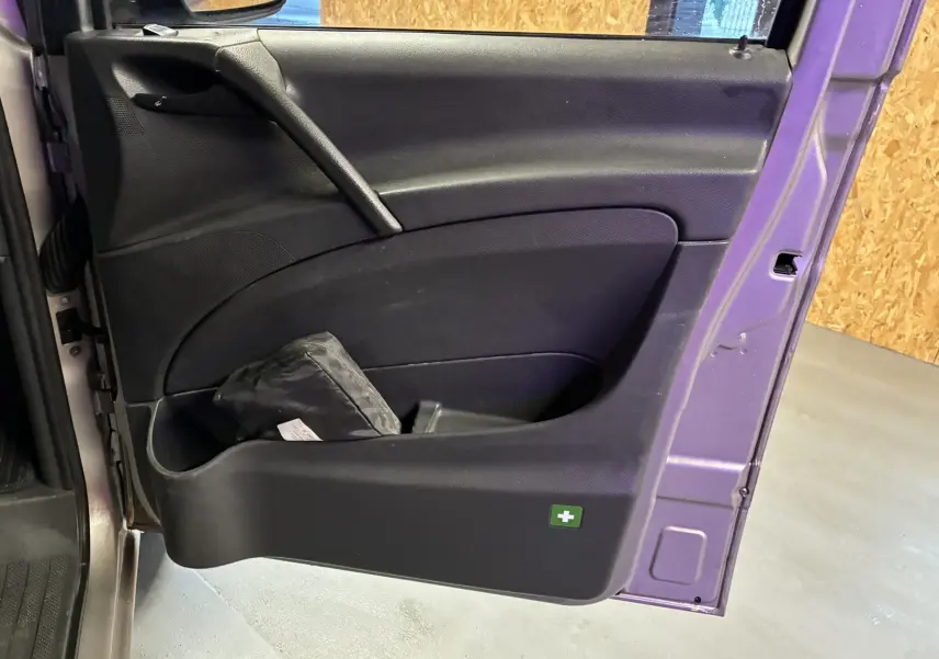 Gros plan sur la porte avant gauche noire du Mercedes Vito gris 2012, avec pochette de secours visible dans le rangement.