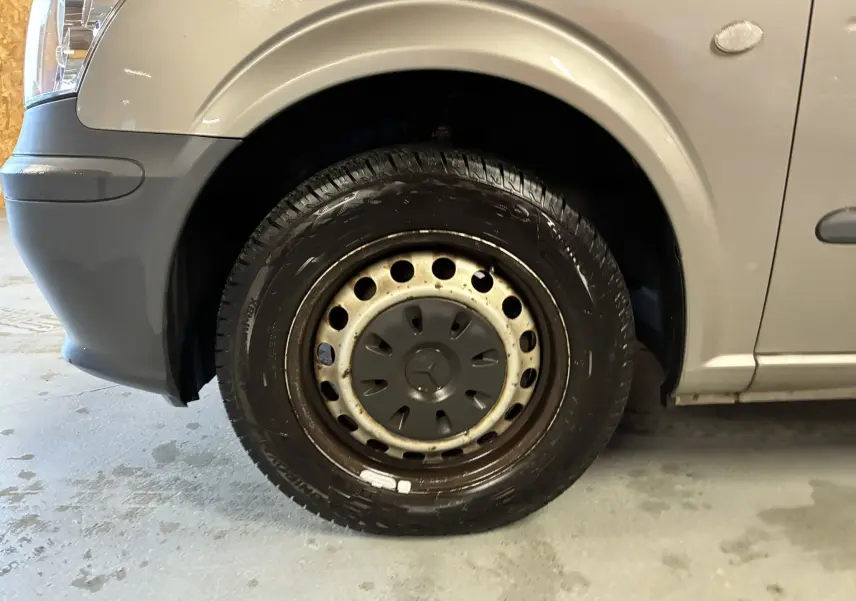 Gros plan sur la roue avant gauche grise d’un Mercedes Vito 2.8 113 CDI Fourgon Long de 2012 avec jante acier et enjoliveur noir.