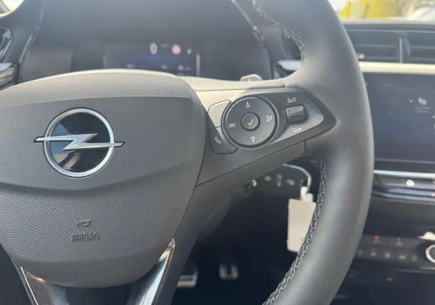 Gros plan sur le volant noir de l’Opel Corsa 2025 avec commandes intégrées et logo Opel central argenté.
