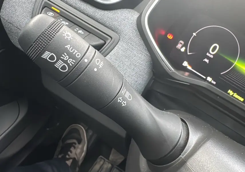 Gros plan sur la commande des feux et le tableau de bord numérique de la Renault Clio gris schiste V TCE 90 Techno Plus 2025.