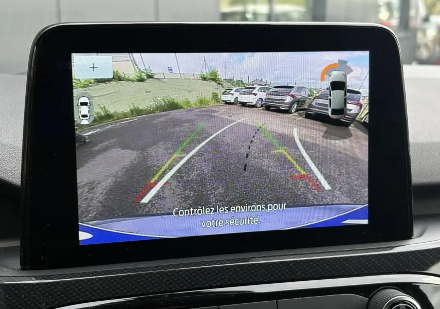 Écran tactile intérieur montrant la caméra de recul du Ford Kuga bleu azur, avec lignes de guidage et vue arrière.