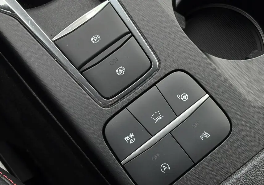 Gros plan sur la console centrale noire du Ford Kuga bleu Azur, montrant les boutons de contrôle électroniques.