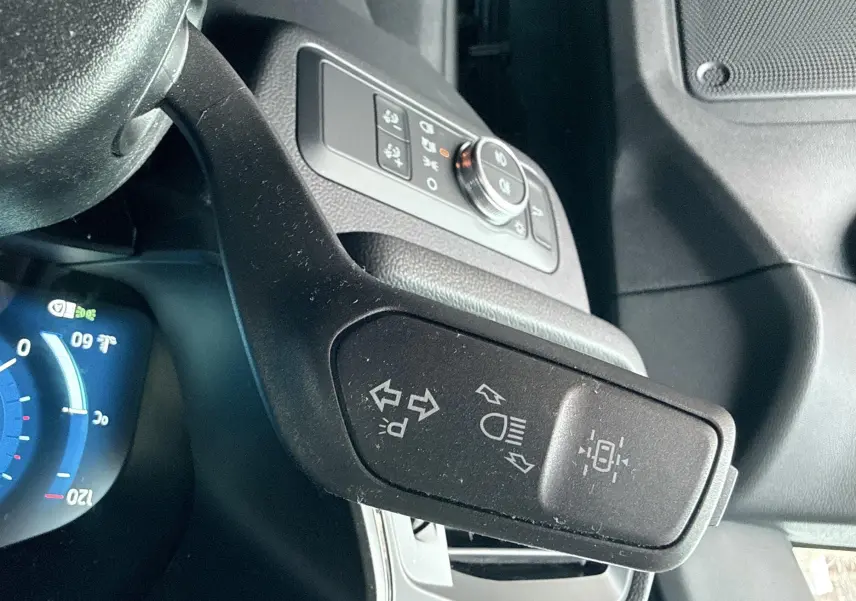Gros plan sur la manette de clignotants noire à gauche du volant dans l'habitacle du Ford Kuga bleu azur 2023.