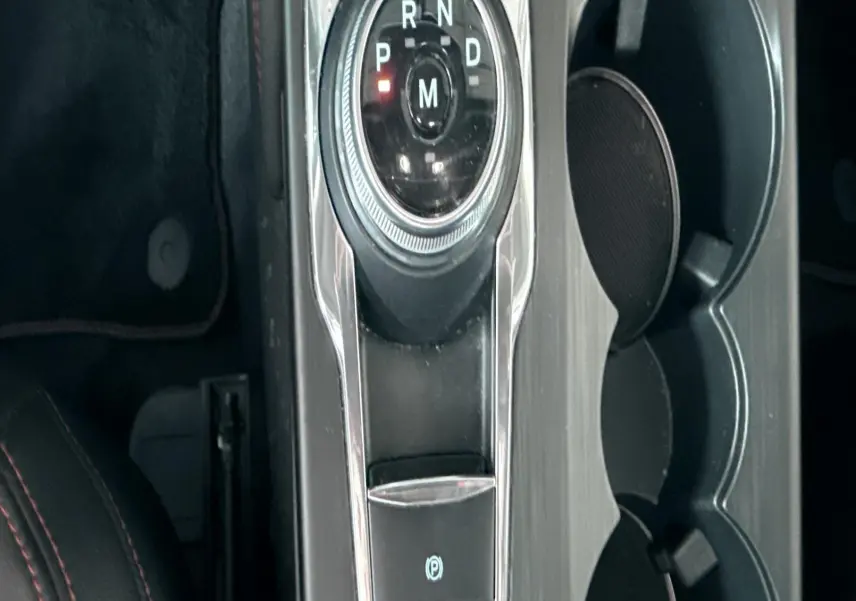 Vue plongeante sur la console centrale noire du Ford Kuga 2023 avec sélecteur rotatif de boîte auto et porte-gobelets.