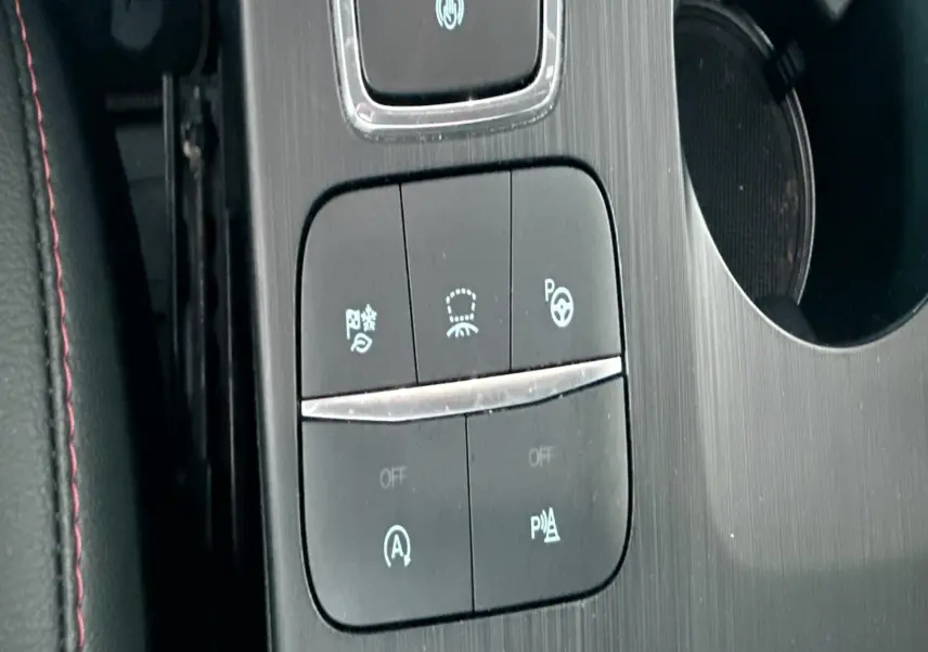 Gros plan sur la console centrale noire du Ford Kuga bleu azur 2023, avec boutons de contrôle et surpiqûres rouges visibles.