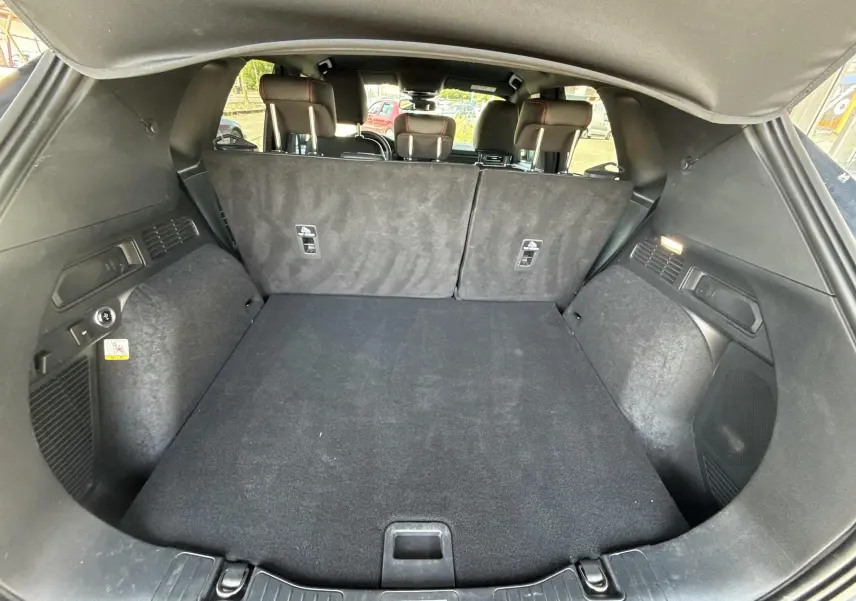 Coffre spacieux ouvert du Ford Kuga bleu azur 2023, avec banquette arrière rabattue et habillage intérieur noir.