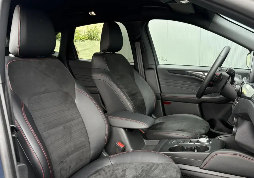 Vue intérieure côté conducteur du Ford Kuga ST-Line X 2023, sièges noirs avec surpiqûres rouges et volant sport à méplat.