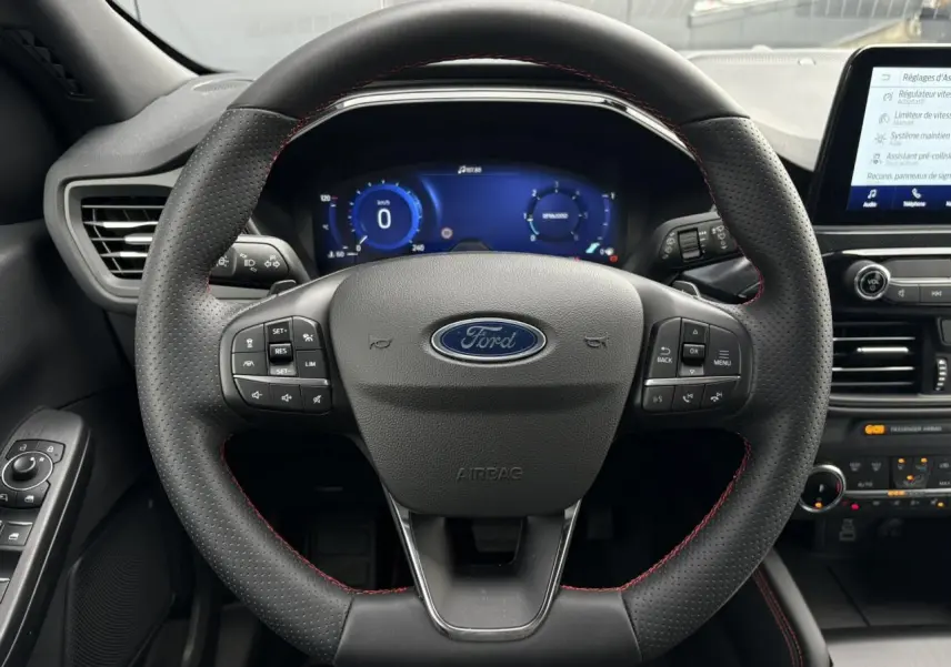 Vue centrée sur le volant perforé noir avec surpiqûres rouges du Ford Kuga 2023, tableau de bord numérique et console tactile visibles.