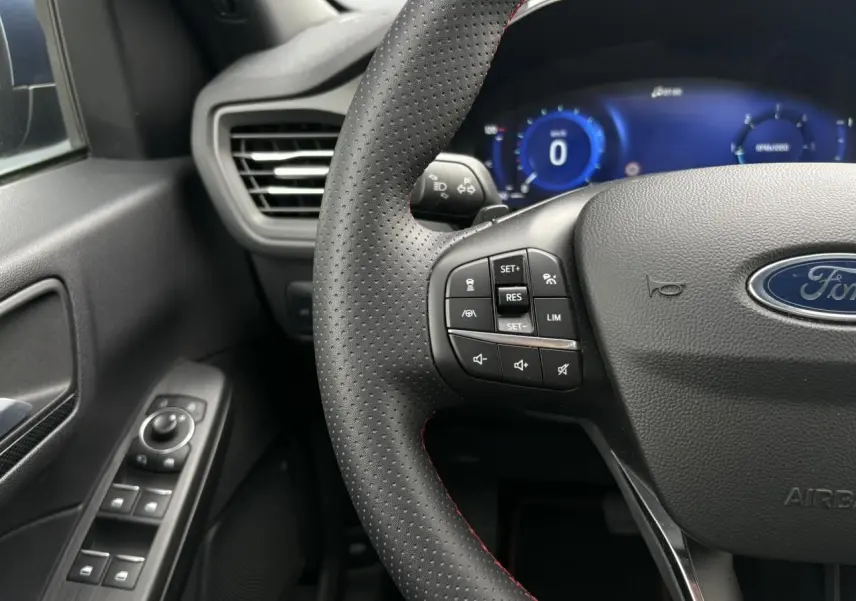 Vue rapprochée du volant perforé noir avec surpiqûres rouges et commandes multifonctions du Ford Kuga 2023.